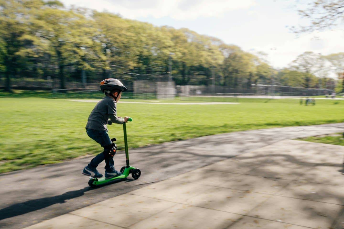 Niño monta patinete verde con desenfoque de movimiento en el parque.