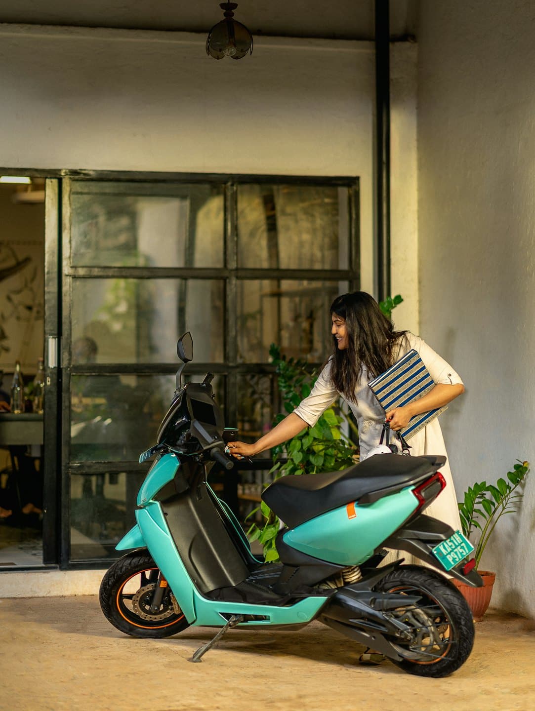 Mujer sonriente con bolso de mano junto a una moto eléctrica turquesa.