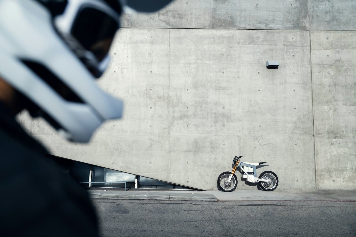 Motocicleta eléctrica blanca aparcada en una acera junto a un muro de hormigón.